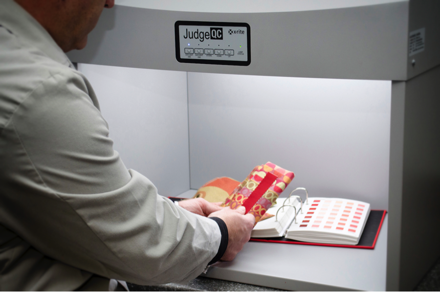 This Quality Control Manager is comparing a textile sample against the color standard in the Judge QC to ensure it is visually correct under different light sources.